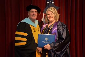 Woman wearing cap and gown receives diploma from man.
