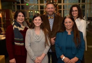 Five students pose in front of a Christmas tree.