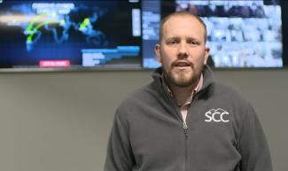 Man stands in front of flat screen displaying world map