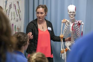 Woman stands next to skeleton, teaching students about therapeutic massage