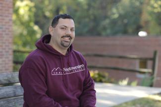 Man sits with SCC fall foliage in the background