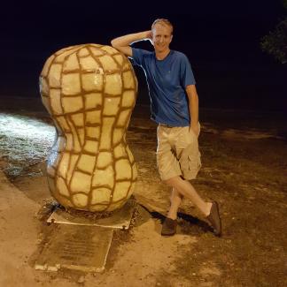 Man stands beside large peanut statue