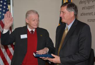 One man holds a Bible as the other places his left hand on the Bible and his right hand in the air to take an oath.