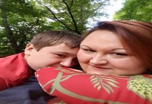 A woman and her son take a selfie underneath some trees outside