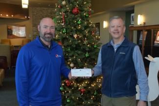 Two men exchange a check in front of a Christmas tree.