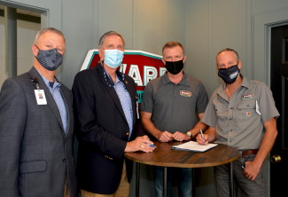 Four men wearing masks stand beside a table.