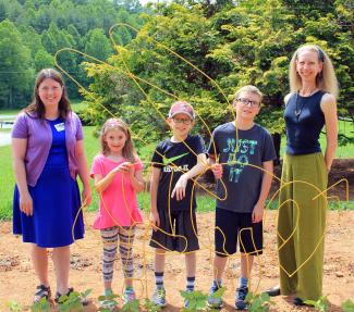 4-H students and Swain Center staff stand with bee sculpture in 4-H learning garden at SCC Swain Center.