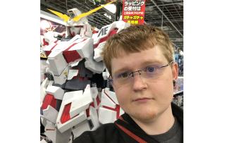 Man stands in front of robot; banner with text in Japanese language is in background