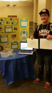 Jonah Caplinger holding first prize certificates standing next to his science project.