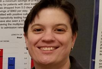 A woman smiles in front of a healthcare research poster