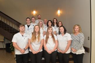 A group of first-year radiography students stand on a staircase in their uniforms alongside female instructor.