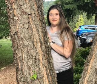 Young woman stands outside against a tree.