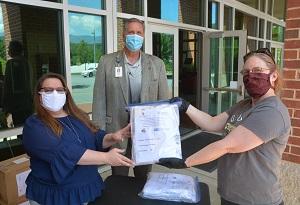 Two women hold up a package of masks while a man stands between them