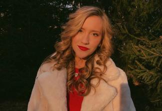 A young woman with blonde hair and red lipstick stands outside for a picture
