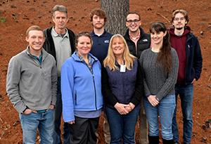 A group of people huddle together underneath a tree on a cold winter day.