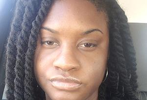 A young woman in a navy sweater smiles in a selfie.