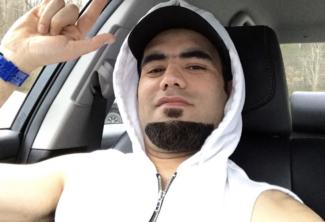 Young man in hoodie sits in his car throwing up playful hand gesture.