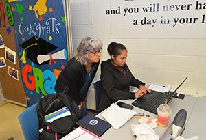 Female instructor leaning over a desk to help female student on a computer.